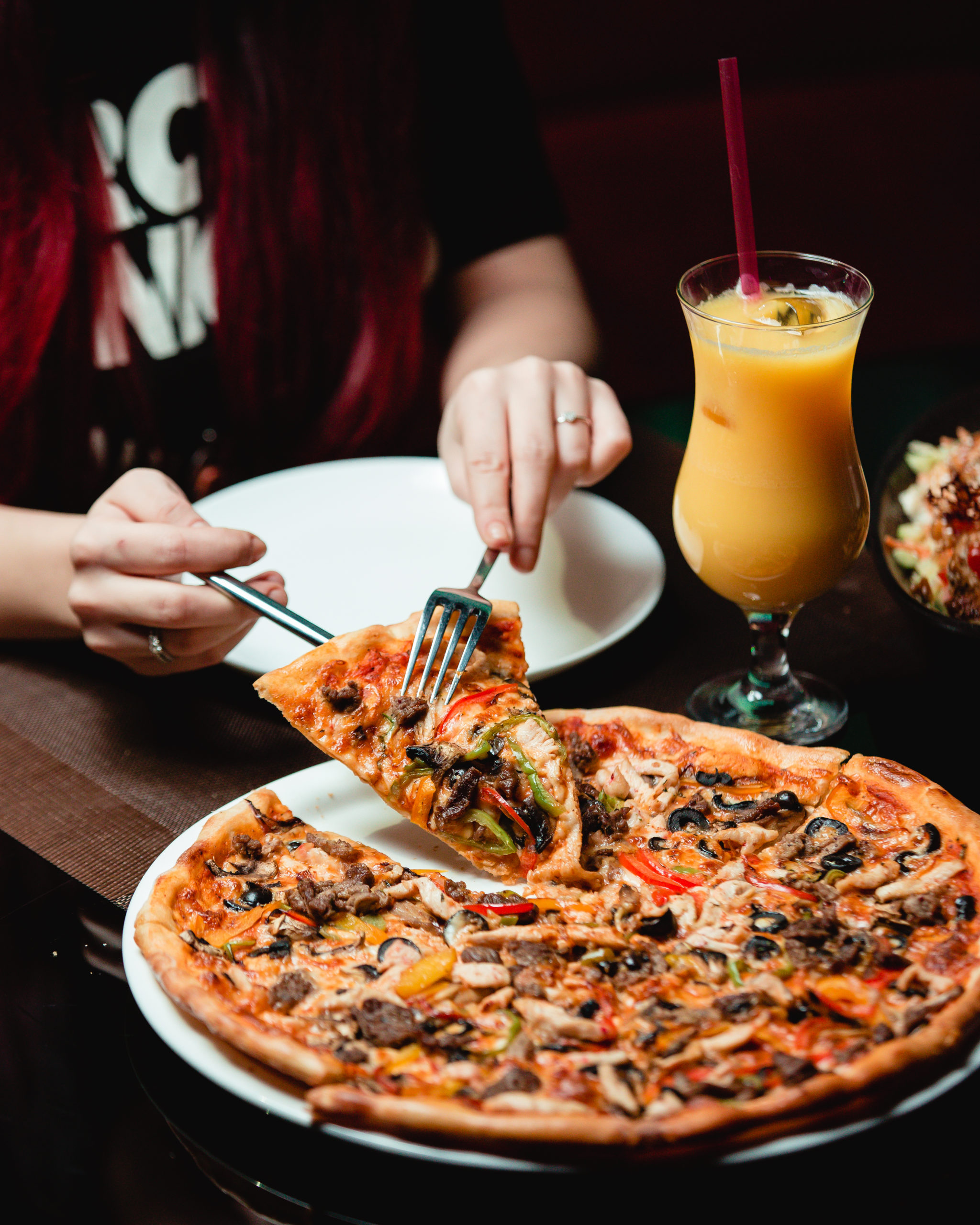 taking-slice-of-mixed-ingredient-pizza-with-glass-of-orange-juice